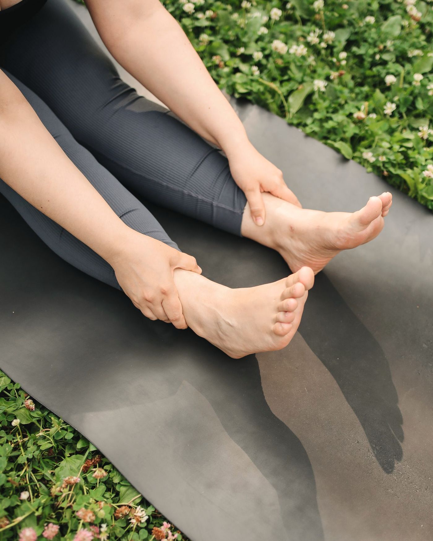Lábfej és szürke leggings jógaszőnyegen, növényzet mögötte